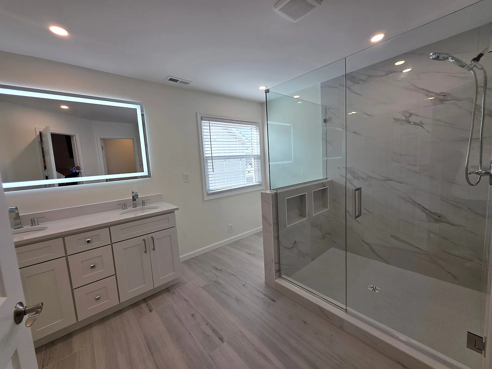 Completed bathroom remodel with tiled walk-in shower, frameless glass enclosure, white vanity, and modern fixtures