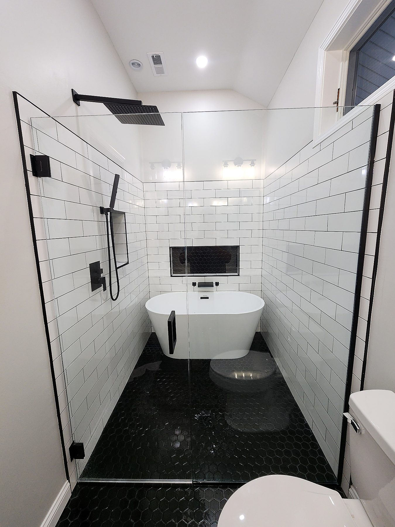 Luxury bathroom remodel with freestanding tub, black hex tile shower floor, and matte black fixtures