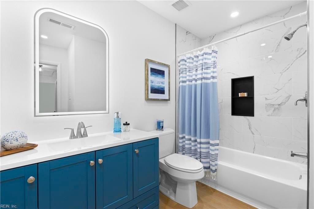 Bathroom remodel with blue shaker vanity, quartz countertop, LED arched mirror, and marble-tile tub shower in Hampton Roads VA