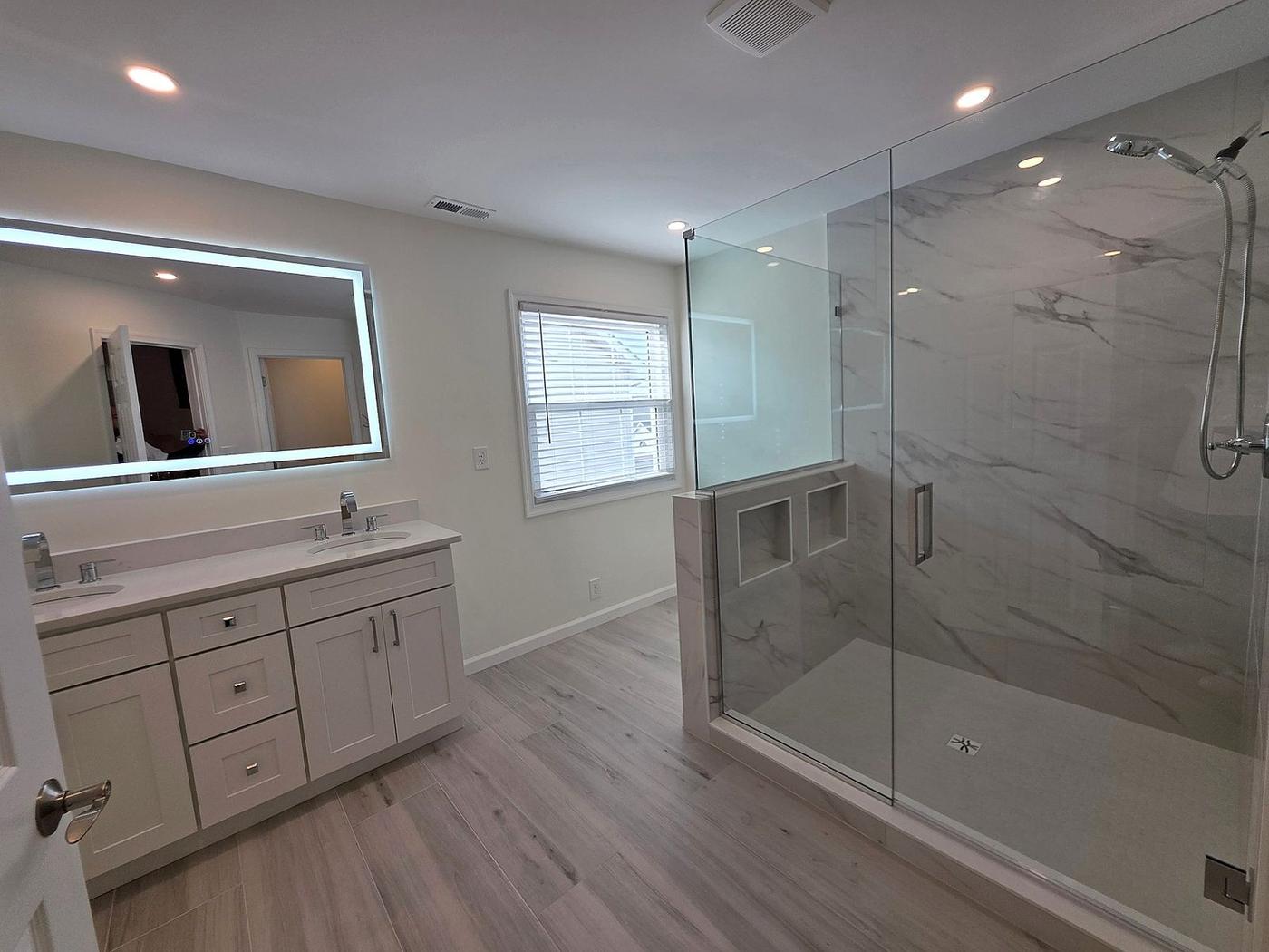 Bathroom remodel with marble-tile half wall, frameless glass shower enclosure, and double vanity area