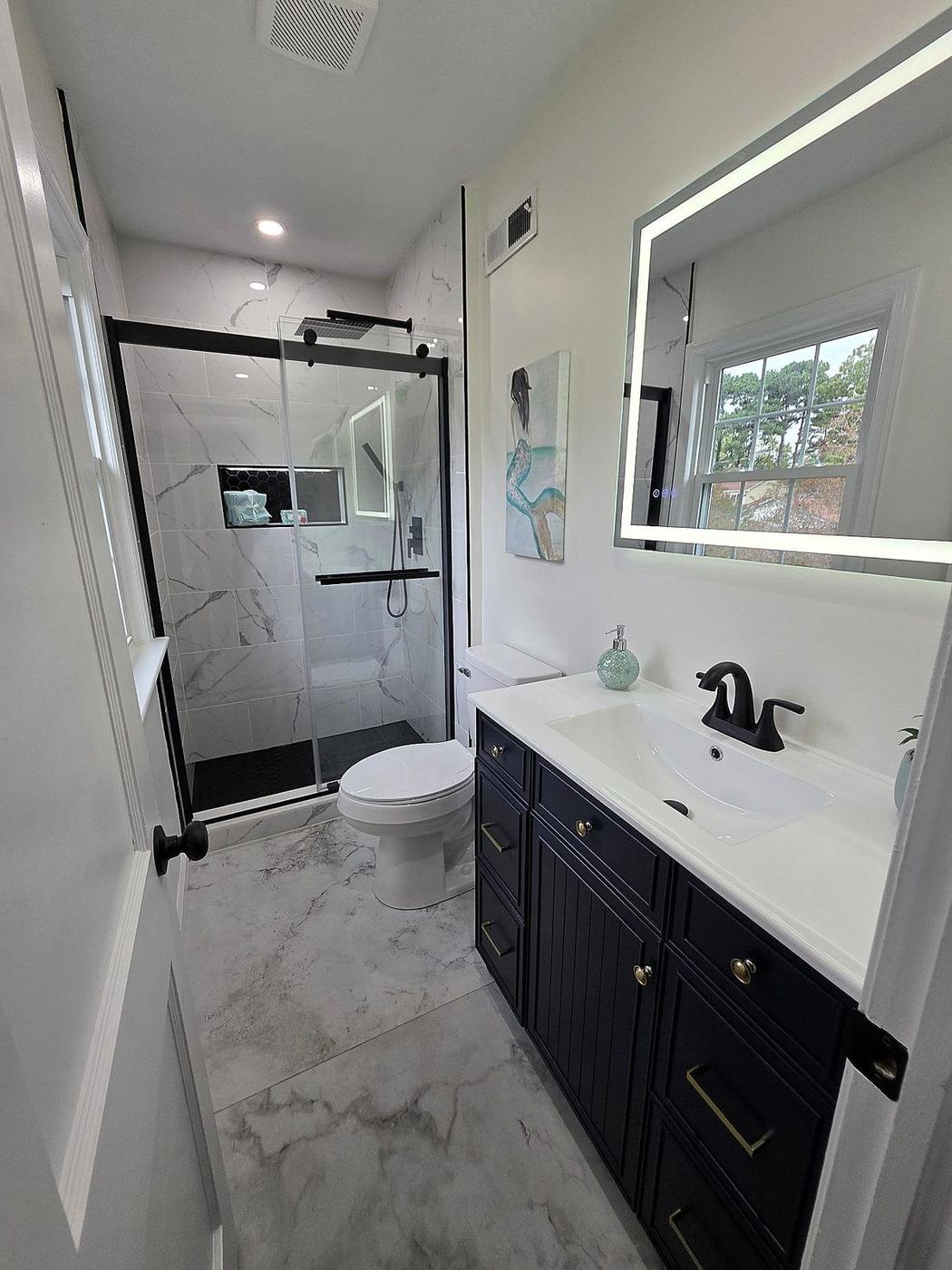 Bathroom renovation with navy vanity, LED mirror, frameless shower glass, and polished tile floors