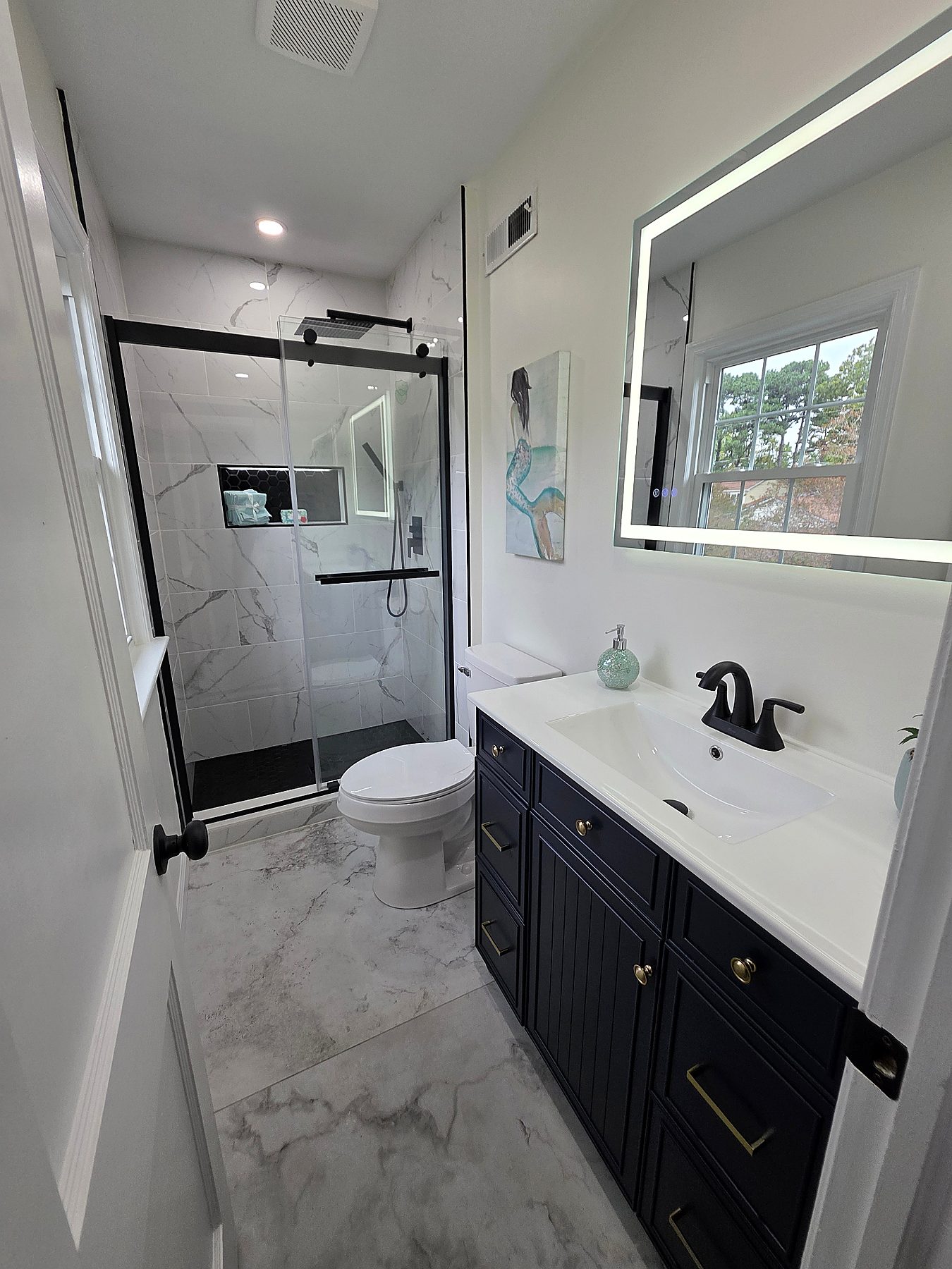 Bathroom renovation with navy vanity, LED mirror, frameless shower glass, and polished tile floors