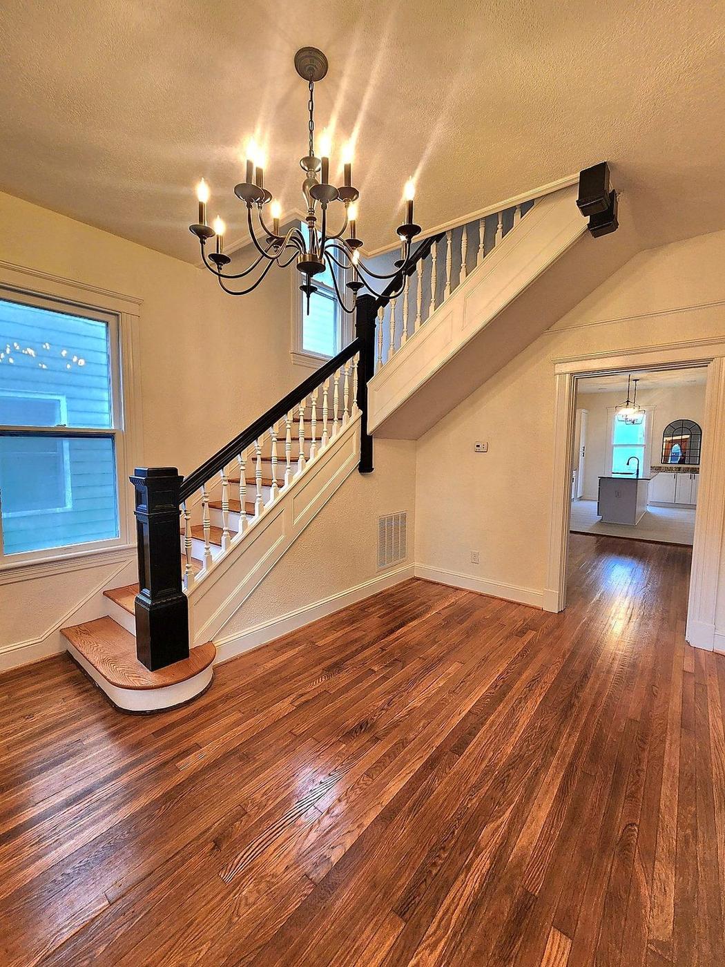 Interior home improvement project with restored hardwood floors, custom staircase trim, and new chandelier lighting