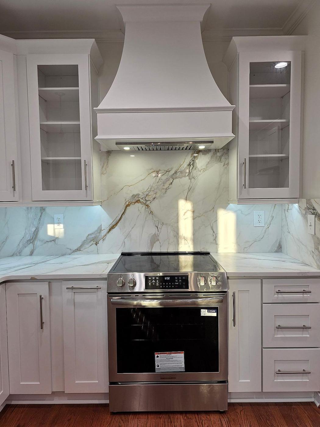 Custom kitchen remodel with decorative range hood, marble backsplash, and white shaker cabinetry