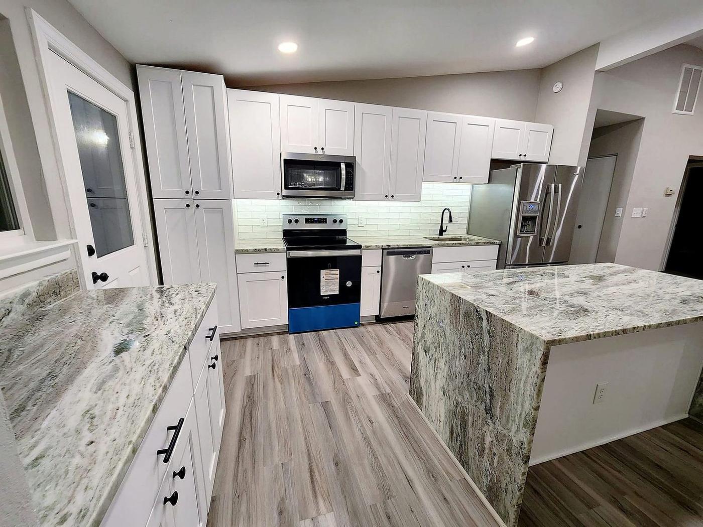 Kitchen renovation with white cabinets, granite waterfall island, stainless appliances, and luxury vinyl plank flooring